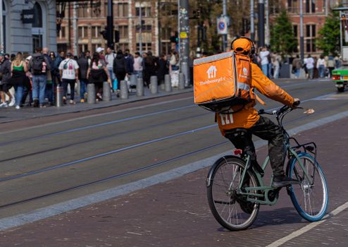 Thuisbezorgd-bezorger met maaltijdtas in een straat in Bestamsterdam tijdens avondlevering
